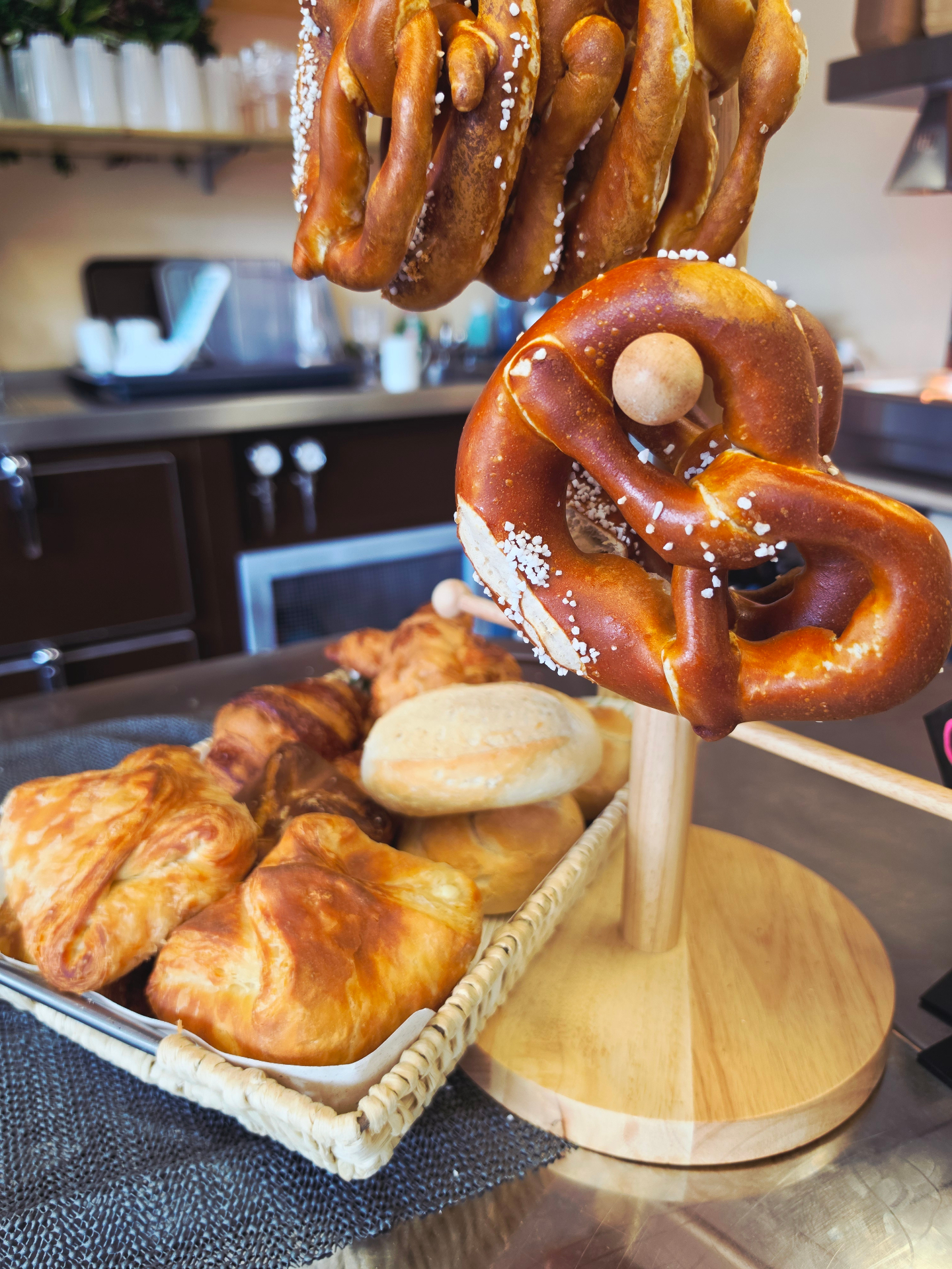 Frische Brezen am Holzständer neben einem Korb mit Croissants und Gebäck