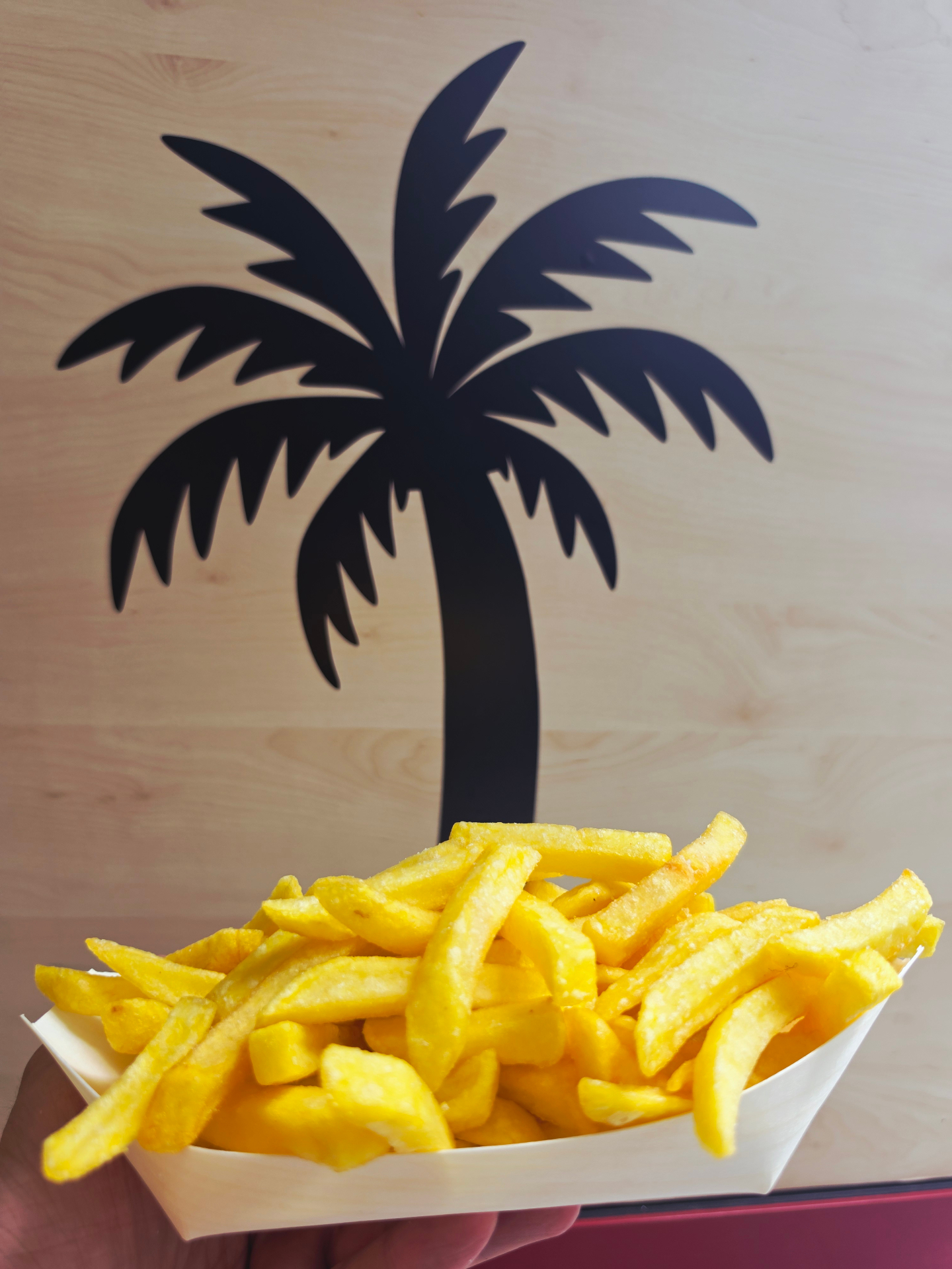 Portion goldene Pommes vor der schwarzen Palmen-Silhouette im Clubbi